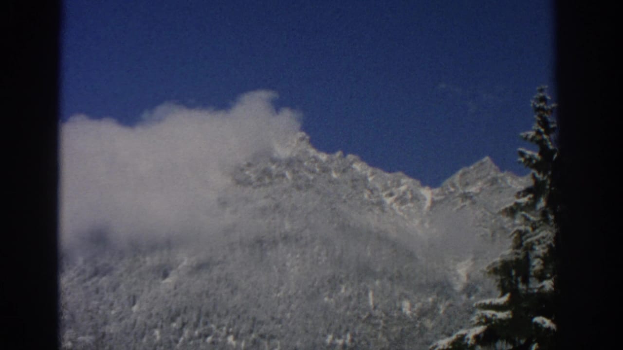Clouds partially cover a snowy mountain ridge under blue sky.
