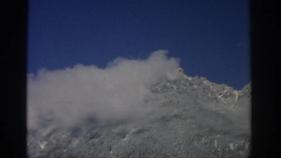 1963 Swiss home-movie frame showing dense white cloud moving across a snowy alpine slope, with only parts of the ridge visible.