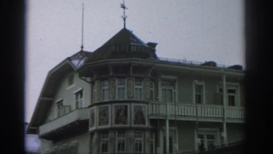 1963 Switzerland home-movie frame of an alpine hotel exterior with ALPENHOF lettering, balcony railings, and painted facade panels.