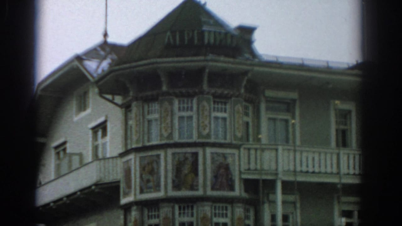 Ornate hotel corner facade with ALPENHOF sign, balcony, and painted panels.