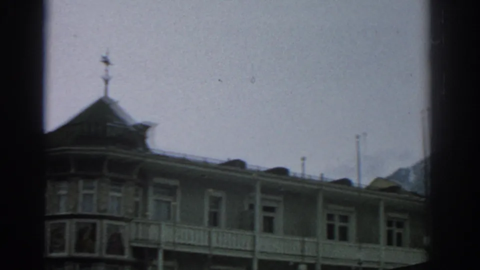 Widest 1963 Zurich frame showing the hotel facade receding across the shot, with balcony rail, windows, roofline, and partly visible ALPENHOF sign.