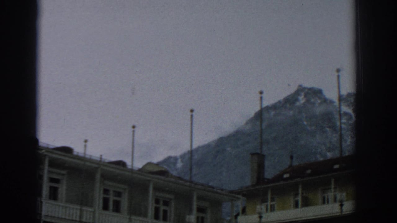Lodge roofs and flagpoles in front of snow-dusted mountain peaks.