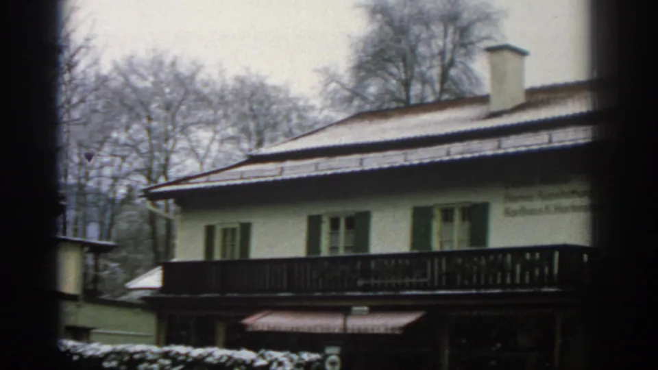 1963 Zurich frame showing a pale building with chimney, shuttered windows, dark balcony railing, and bare trees under an overcast sky.