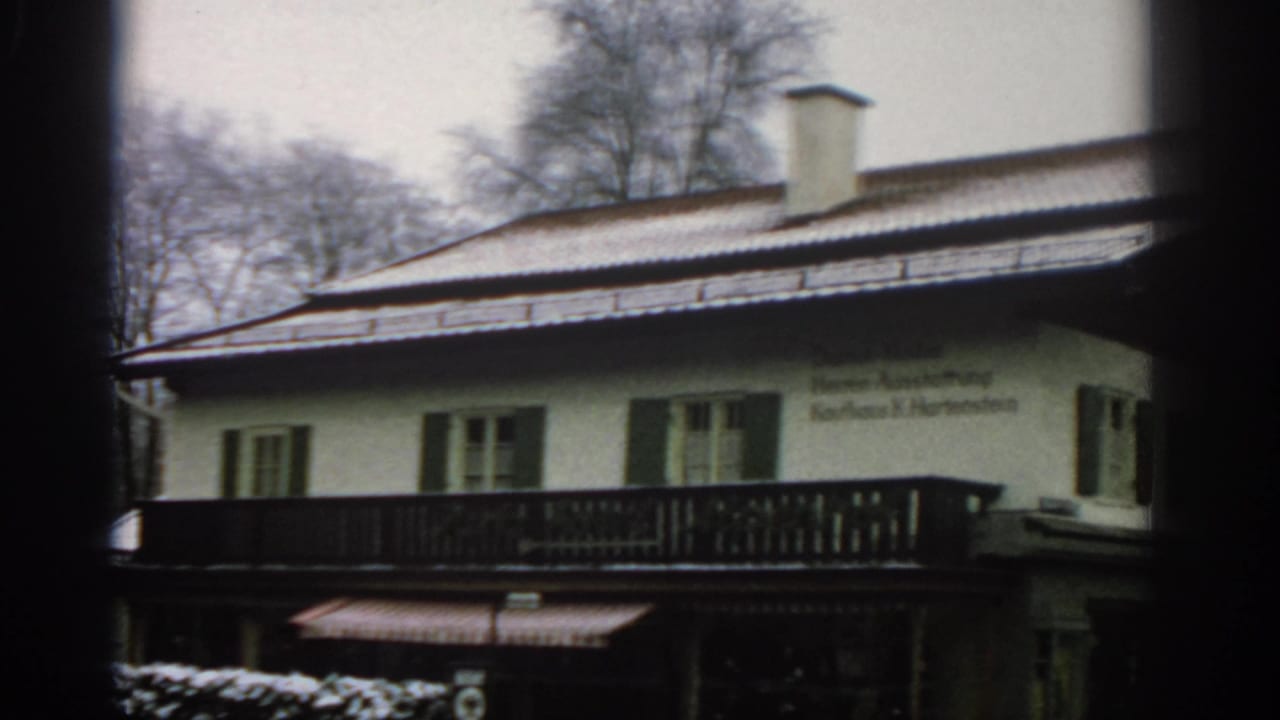 Snow-dusted Alpine-style building with green shutters, balcony, and wall text.