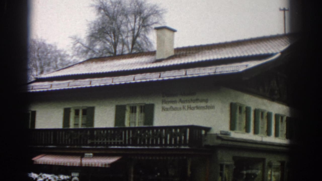 White building exterior with snow on the roof, green shutters, and German text.