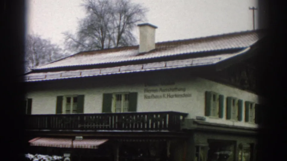 1963 Zurich frame of a snow-covered roof and white facade with green shutters, balcony railing, and German text on the upper wall.