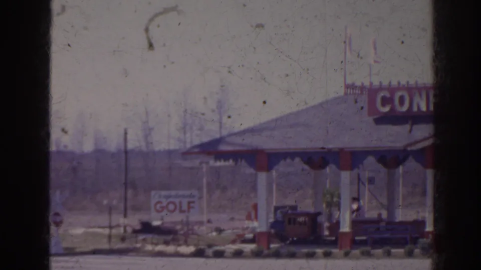 1962 Florida 8mm frame showing a covered attraction pavilion with red and white pillars, partial CONFEDERATE signage, a golf sign, and a small train or trolley.