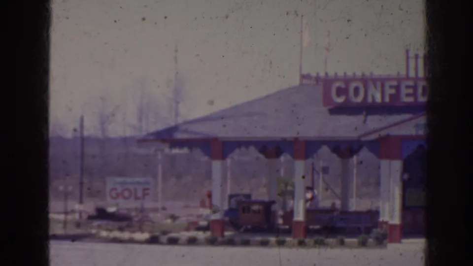 1962 Florida home-movie frame with a cropped view of a pavilion, partial CONFEDERATE lettering, a golf sign in back, and a small train or trolley below.