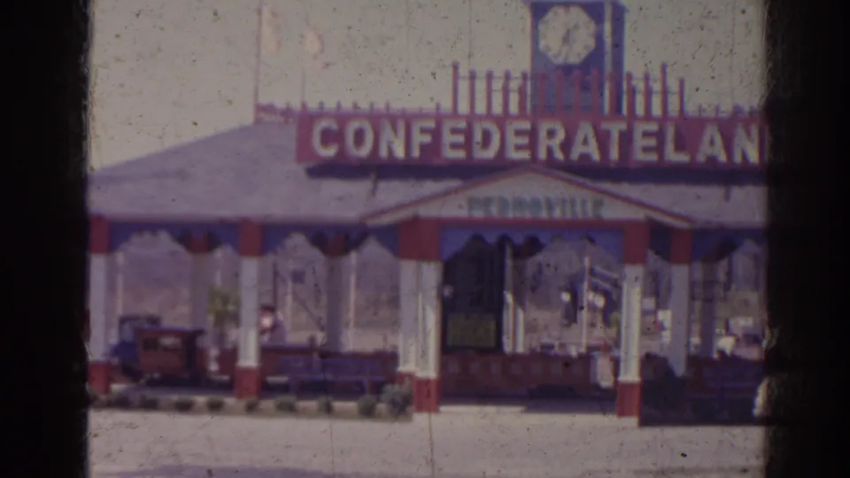 1962 Florida frame showing a pavilion marked CONFEDERATE LAND, with a clock tower, small train cars, and a distant person near the right edge.