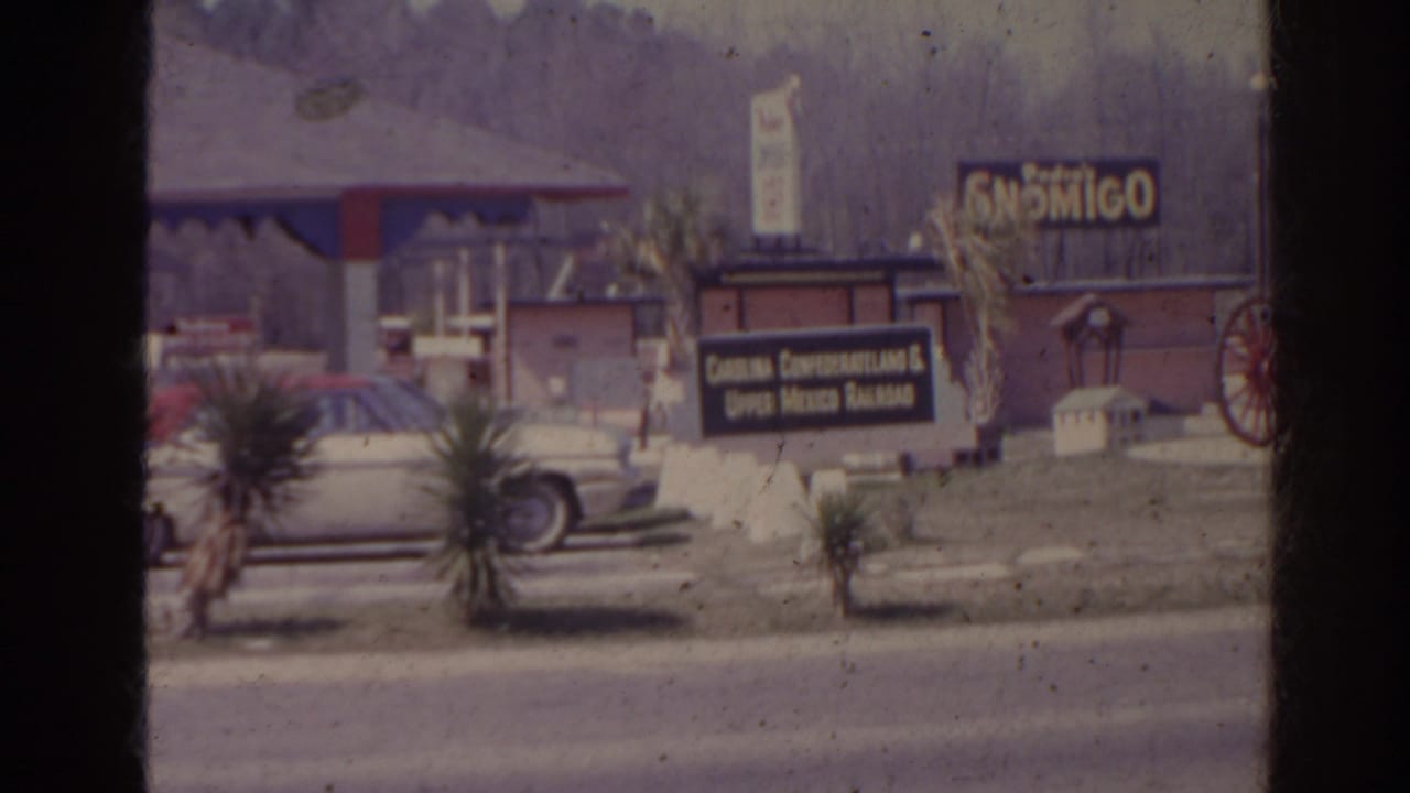 Roadside scene with gas station canopy, parked car, Son Migo sign, and a small restaurant sign.