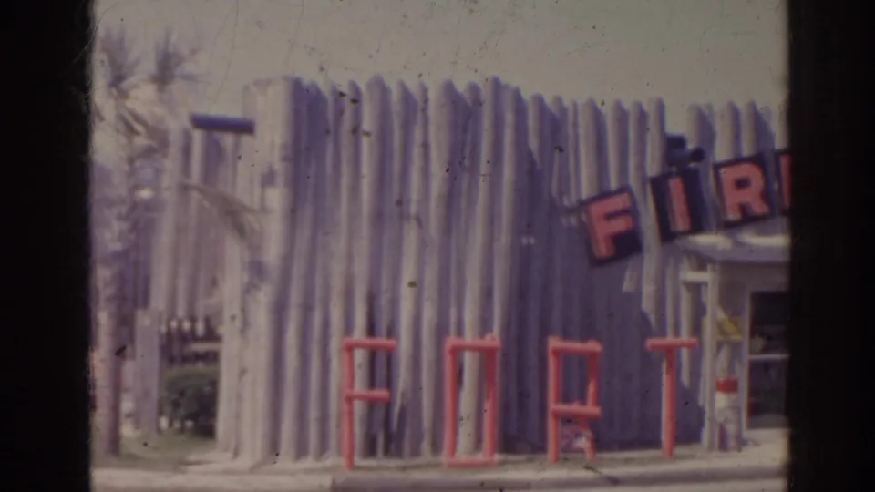 1962 Florida frame showing a log-cabin style roadside storefront with partial FIRE lettering and large red FORT letters across the front.