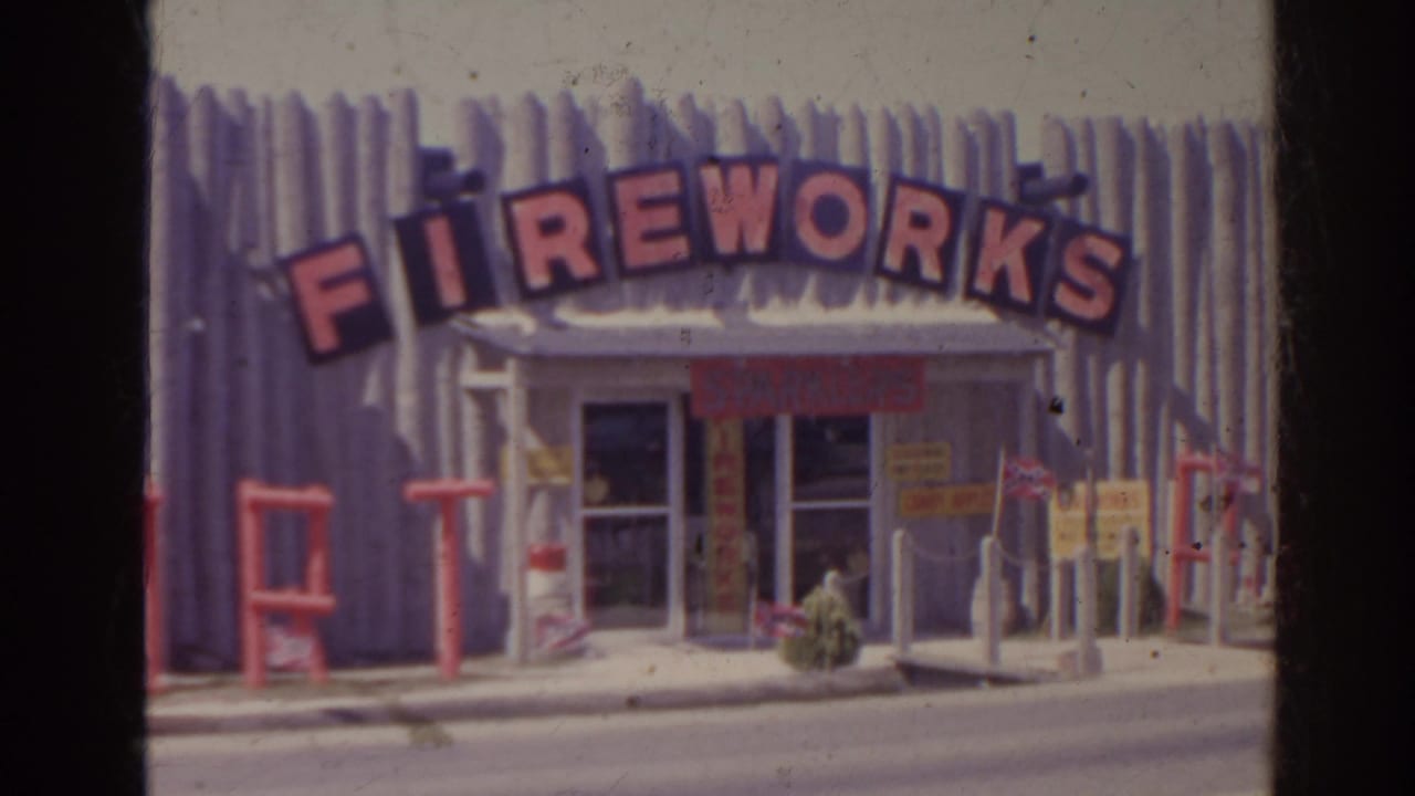 Fireworks shop front with red arched sign, metal siding, glass doors, and signs near the entrance.