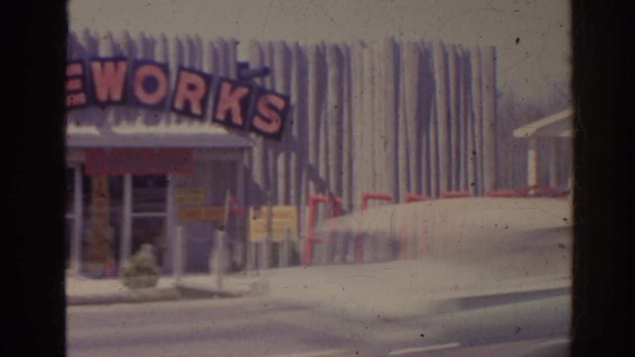 Roadside storefront with large red FIREWORKS sign and a blurred car passing in front.
