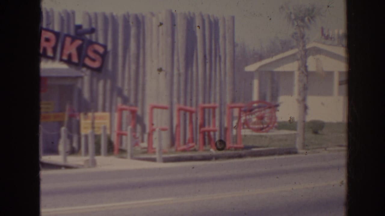 1962 Florida roadside view of Fort Pedro with FIREWORKS signage, a red fence or railing, and a small white pavilion.