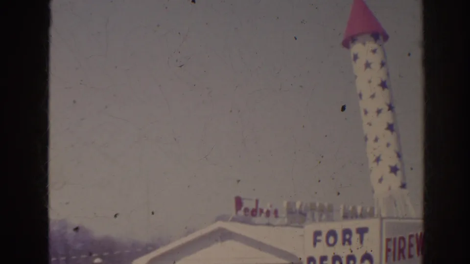 1962 Florida 8mm frame with a tall star-covered rocket sign above the Fort Pedro building and partial fireworks lettering.