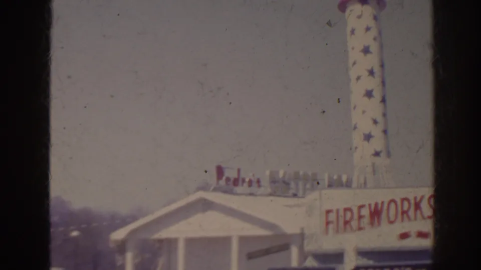 1962 Florida home-movie frame showing the Fort Pedro Fireworks building with a tall novelty rocket sign at the roadside.