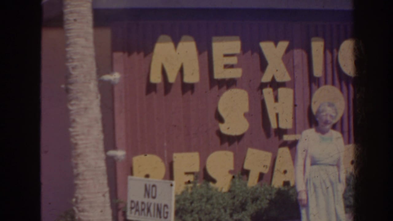 Woman in a light dress stands near a Mexico Shop Restaurant wall and no-parking sign.