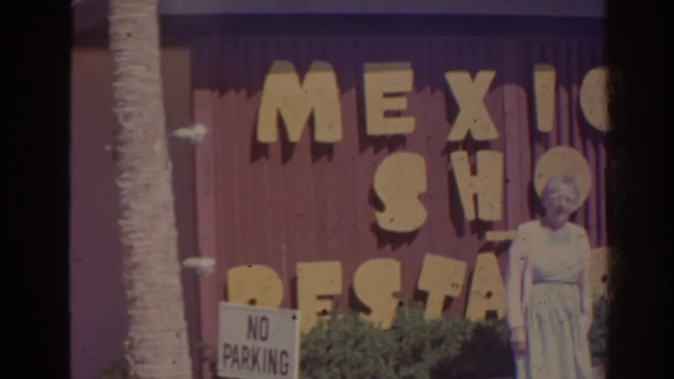 1962 Florida home-movie frame with a woman posing outside a Mexico Shop Restaurant exterior beside a no-parking sign.