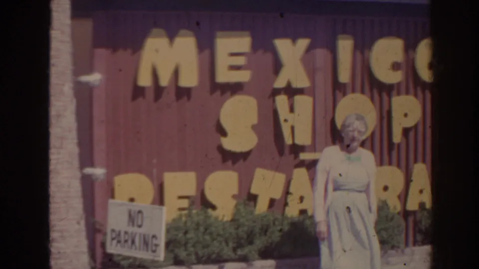 1962 Florida 8mm frame showing a woman posing in front of large yellow Mexico Shop Restaurant lettering on a purple wall.