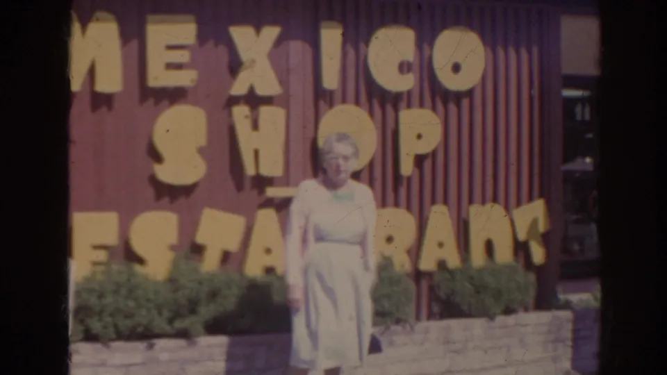 In 1962 Florida home-movie footage, an elderly woman poses outside a red roadside building marked Mexico Shop Restaurant.