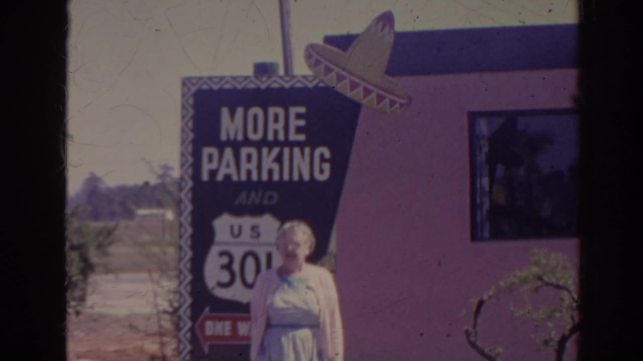 Elderly woman near a blue More Parking sign with a U.S. route shield and sombrero decoration.