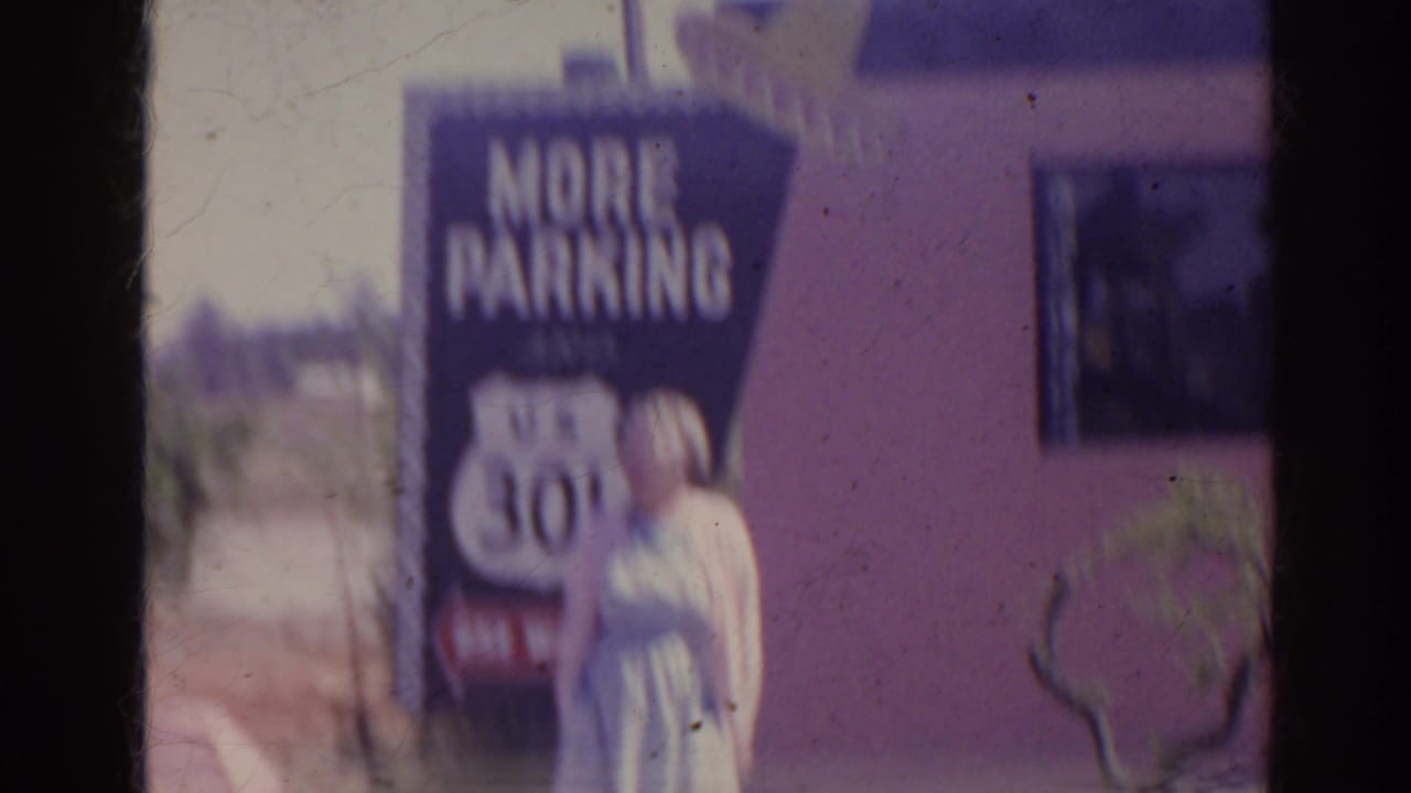 1962 Florida home-movie frame showing a woman beside a roadside parking sign with US 301 text near a pink building.