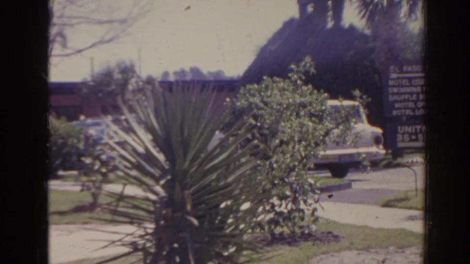 1962 Florida motel parking view with yucca-like planting, shrubs, a white sedan, and a partially visible El Paso Inn sign.