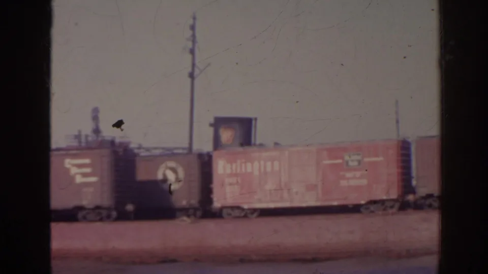1962 Florida 8mm frame showing red freight boxcars on a low brown barge beside a waterfront with utility poles.
