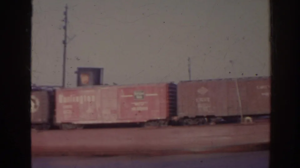 1962 Florida home-movie frame of boxcars on a barge, with railroad lettering visible and utility poles in the background.