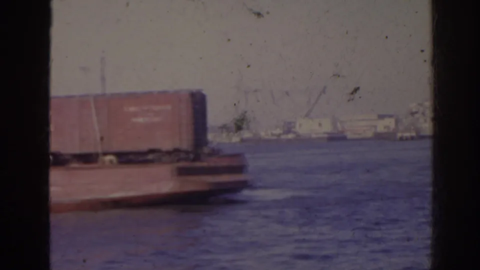1962 Florida home-movie frame of the barge end, a freight car, open water, and distant waterfront structures.