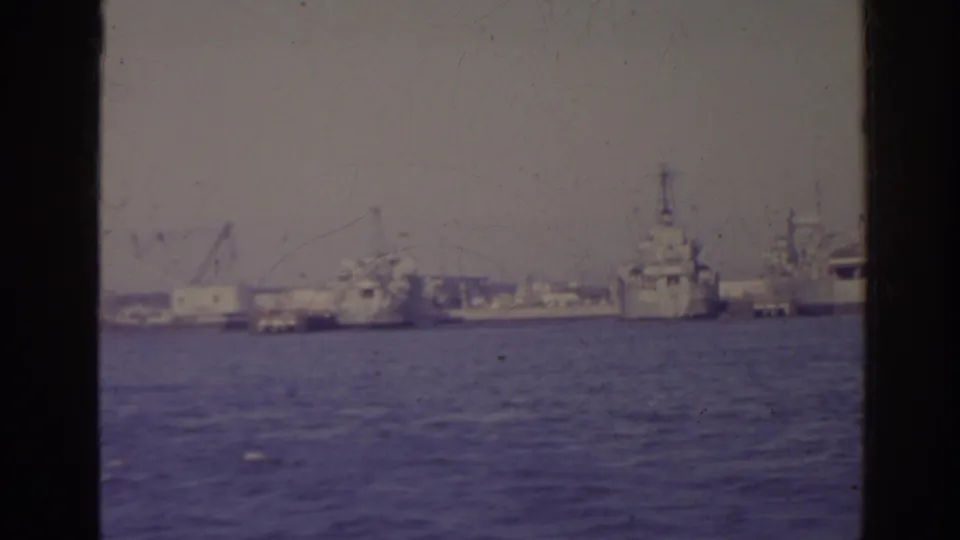 1962 Florida waterfront with harbor water in front, docked naval-looking ships, cranes, and industrial structures seen through dark vertical edges.