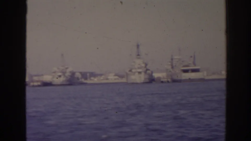 1962 Florida harbor frame showing a large naval-looking vessel, dockside cranes, industrial buildings, and water in the foreground.