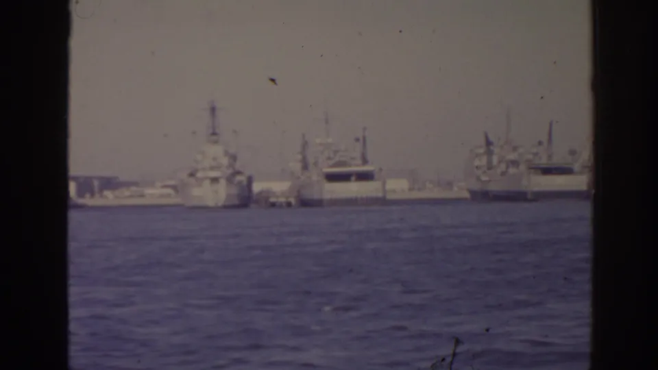 Distant 1962 Florida harbor view with multiple naval vessels and larger transport-like ships seen across open water.