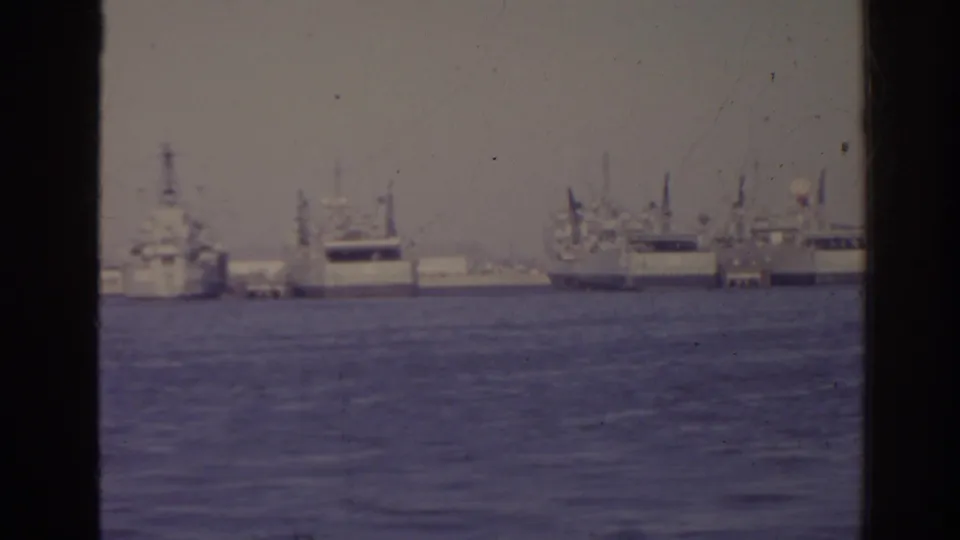 Soft 8mm frame from Florida in 1962 showing anchored naval ships across rippled harbor water with faded color and scratches.