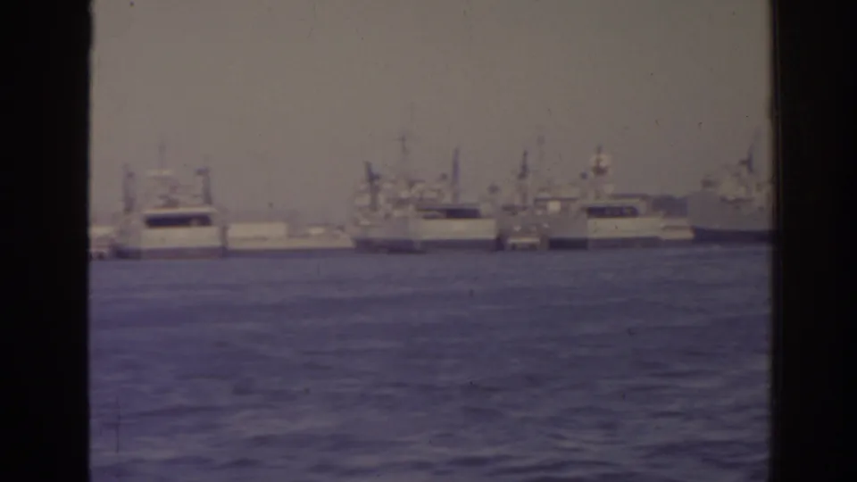 1962 Florida harbor frame showing a distant line of naval ships and support vessels across blue water, bordered by the scanned film edge.