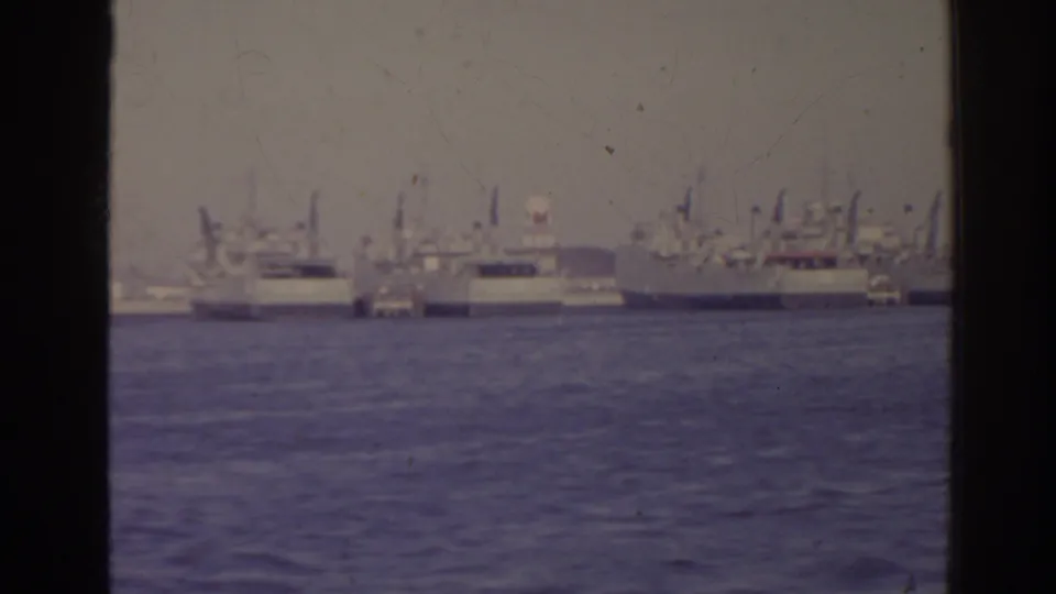 Distant 1962 Florida harbor view with large ships, masts, and low waterfront structures across the water.
