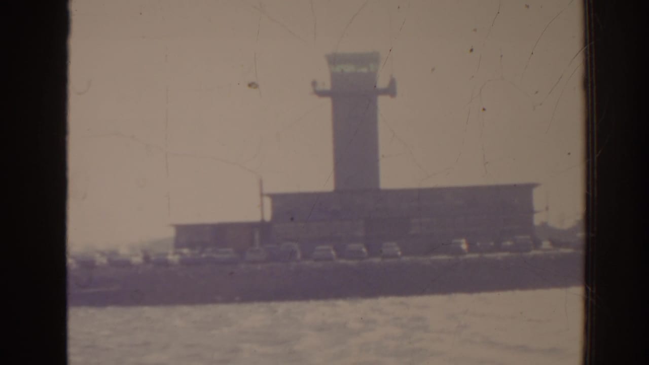 Harbor tower and waterfront seen through a dark window frame beside water.