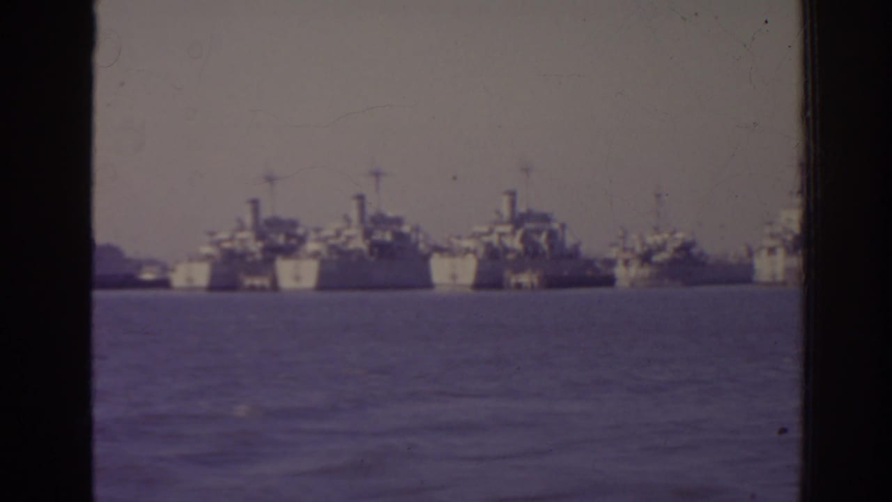 Distant naval ships anchored across harbor water behind a window frame.