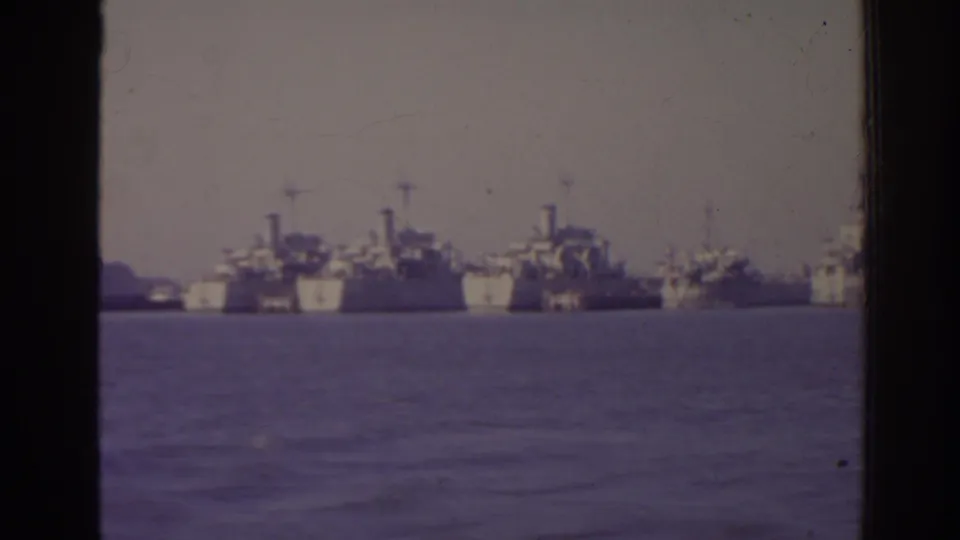1962 Florida 8mm view of multiple naval ships anchored in a hazy harbor, partly divided by the dark frame of the filming position.