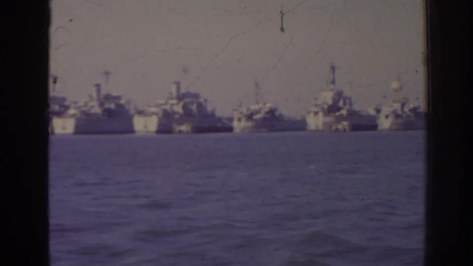 1962 Florida home-movie frame showing several distant naval vessels across open harbor water, with soft focus and aged color film texture.