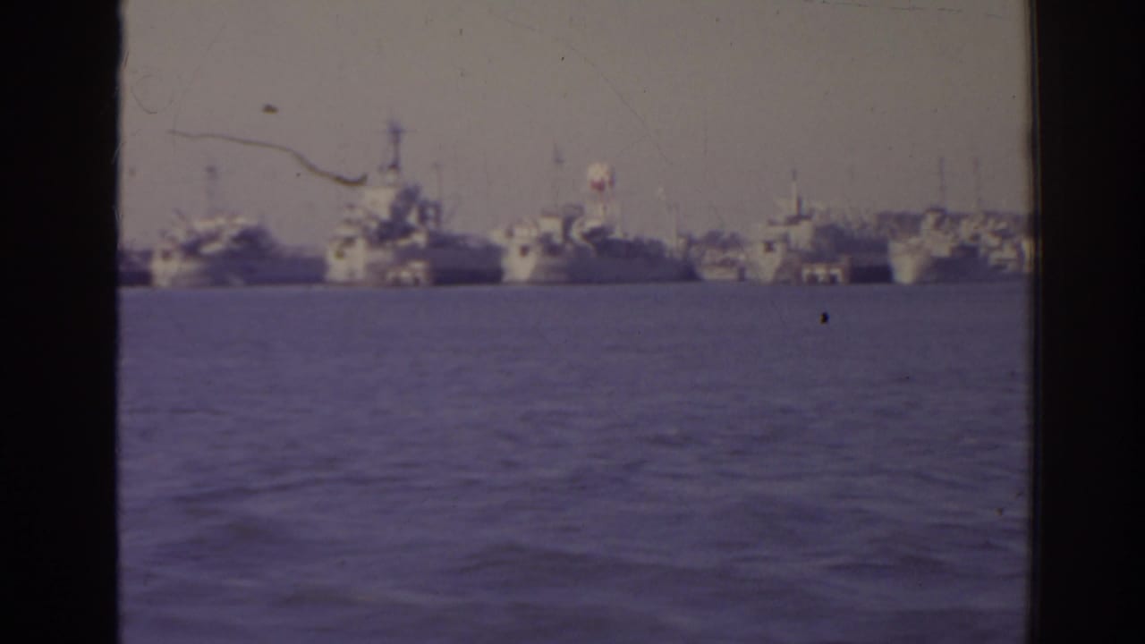 Distant naval ships across harbor water seen through dark window framing.