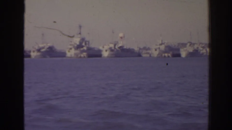 1962 Florida 8mm frame showing distant naval ships at anchor across harbor water, partially divided by dark window framing.