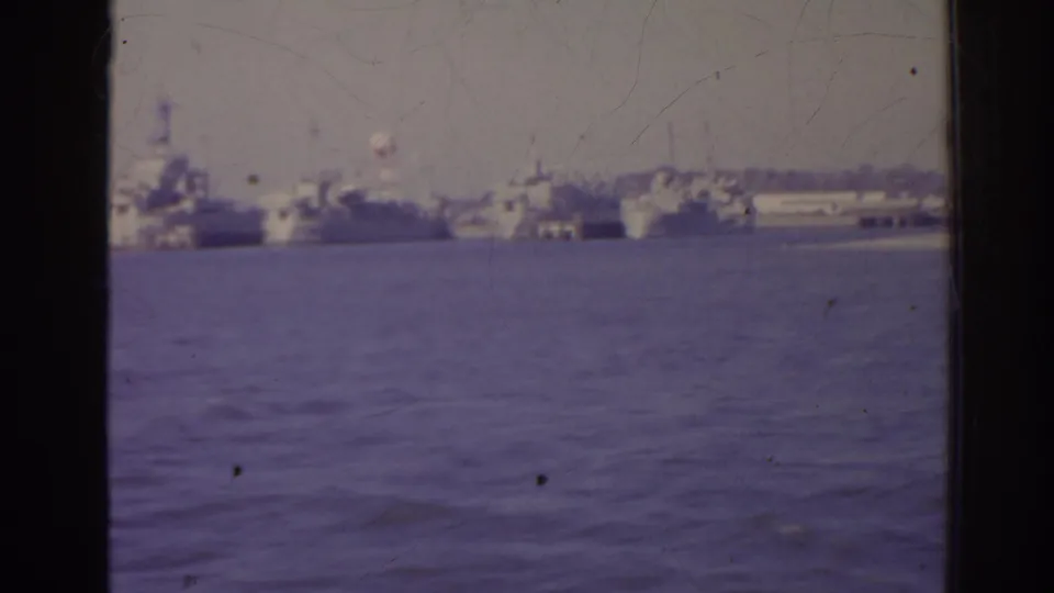 1962 Florida home-movie view of anchored ships across calm harbor water, with a dark vertical frame edge in the foreground.