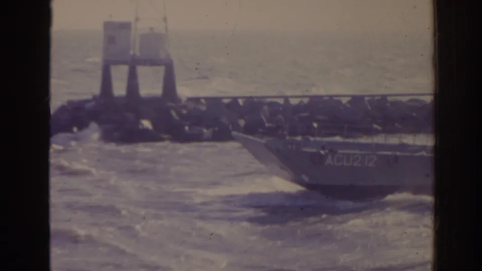 1962 Florida 8mm frame with landing craft marked ACU212 moving past a rocky jetty under hazy light.