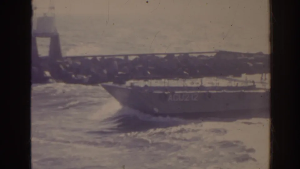 1962 Florida 8mm frame showing the side of the ACU212 landing craft against jetty rocks and rough water.