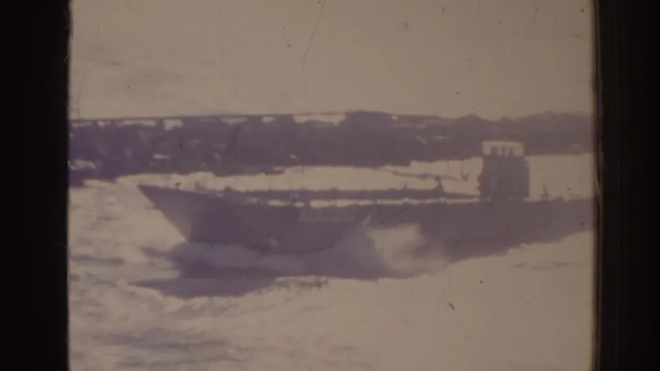 1962 Florida 8mm frame showing the ACU212 landing craft moving beyond the jetty with wake and distant shore visible.