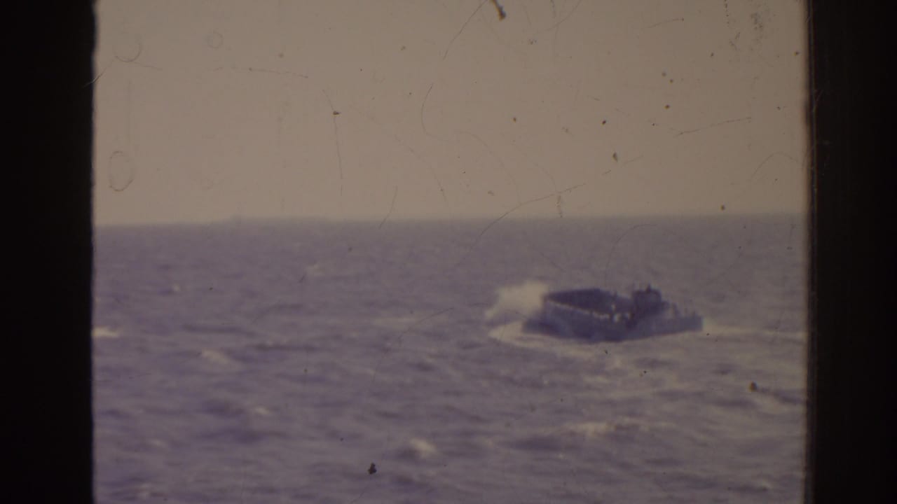 1962 Florida 8mm frame showing a small military-style craft in rough seas with white spray and faded color.