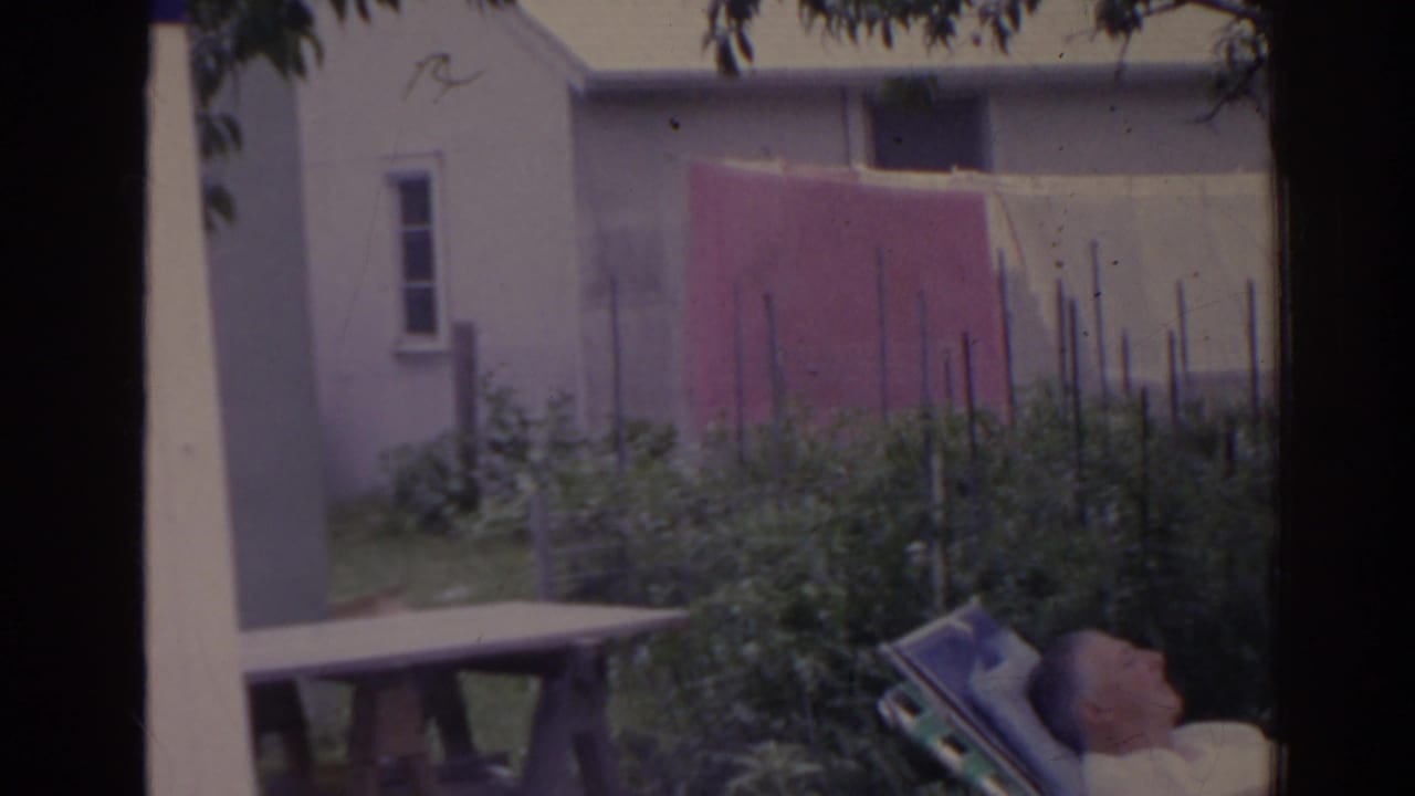 Elderly man reclining in a backyard garden with laundry on a clothesline behind him.