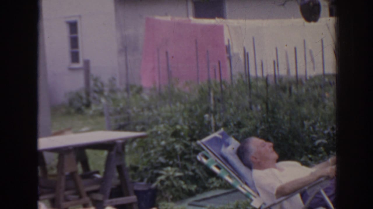 Man reclining at the edge of frame with a backyard garden, picnic table, and clothesline visible.