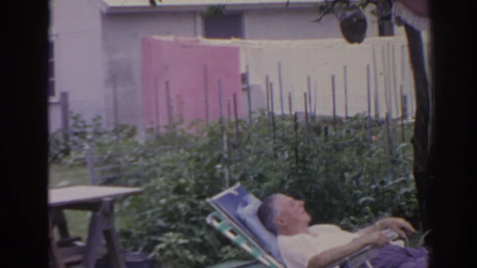 1962 Florida 8mm frame showing the backyard garden and clothesline, with the reclining man low in the frame.